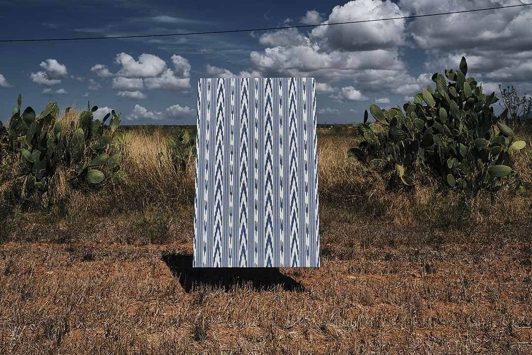 Blue and white Mallorcan ikat by Teixits Riera hung outdoors among cactus and dry grass